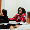 A female student in a red jacket smiles during a class discussion.