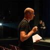 A man holding a pen and notebook looking at activity on stage.