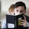 A male student's face is obscured by the book he is reading.